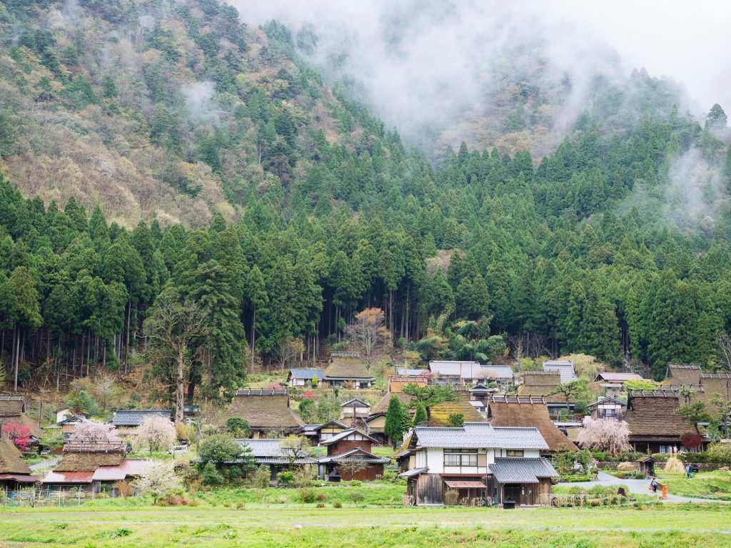 A picturesque rural Japanese village nestled at the base of misty, forested mountains. This scenic countryside features traditional thatched-roof kominka homes and seasonal cherry blossoms, offering a timeless glimpse into old Japan. Perfect for travelers, property hunters, and anyone interested in Japanese akiya houses, off-grid living, and peaceful nature retreats in Japan.
